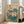 May include: A framed vintage Japanese botanical print featuring white lotus flowers with teal blue-green leaves against a cream background. The artwork shows delicate line work in traditional Asian style with Japanese characters and a red seal in the upper right. The print is displayed in a light wooden frame leaning against a white wall next to a beige upholstered chair in a bright, minimalist living room with white walls and wooden flooring.