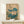 May include: Japanese botanical art print in light wooden frame showing white lotus flowers with large teal-blue leaves against cream background. Print displayed on pale wooden console table with small white wrapped gift box. Traditional Asian calligraphy visible in upper right corner. Minimalist home decor setting with white walls and soft natural lighting.
