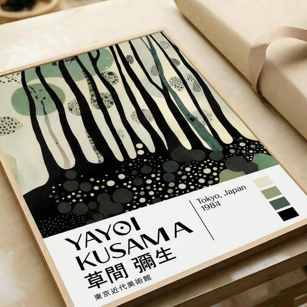 May include: Abstract art poster with black vertical dripping lines over cream background, dotted green circular shapes in upper portion, black dotted ground area below. Features Japanese text and "Tokyo, Japan 1984" with small color palette squares. Displayed in light wood frame on beige fabric surface next to rolled paper.