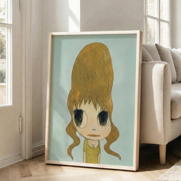 May include: Large framed artwork leaning against beige sofa in bright living room with white walls and windows. Art shows anime-style character with oversized blonde beehive hairstyle, large dark eyes, and yellow dress on mint green background. Light wood frame, displayed on hardwood floors with natural lighting.