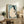 May include: Japanese woodblock print style artwork in light wood frame showing nude woman with long black hair combing her hair against turquoise background. Print displayed on rustic wooden sideboard with books, ceramic vases, fern plant, and leather armchair visible in warm-toned living room setting.