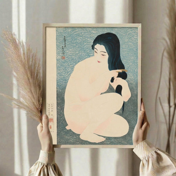 May include: Person in cream ruffled sleeves holding framed Japanese woodblock print depicting woman with black hair combing her hair, seated nude figure against blue-green textured background with traditional calligraphy and red seal stamps, other hand holds dried wheat stalks, soft natural lighting near white curtained window
