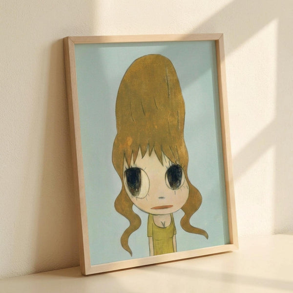 May include: Framed art print leaning against white wall with natural light shadows. Features anime-style character with oversized golden blonde beehive hair, large dark eyes, and yellow-green outfit on soft blue background. Light wood frame, approximately 8x10 size, positioned at slight angle showing dimensional depth.