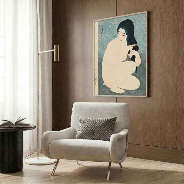 May include: Japanese woodblock print artwork displayed in modern living room setting with beige armchair, brass floor lamp, and wood paneling. The vintage poster shows a seated nude woman with black hair against turquoise background in traditional ukiyo-e style, framed in light wood frame.