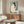 May include: Japanese woodblock print showing woman with long black hair combing her hair, seated nude against turquoise background, displayed in thin gold frame above mid-century walnut credenza. Modern living room setting with white curved chair, brass floor mirror, white table lamp, and glass coffee table on area rug.