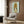 May include: Framed poster artwork featuring anime-style character with oversized blonde beehive hairstyle and large eyes on light blue background, displayed above beige upholstered armchair with geometric patterned pillow in modern living room with wood paneled walls, brass floor lamp, and side table with open book.