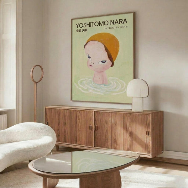 May include: Framed poster featuring child-like figure with orange cap emerging from green rippled water against pale background, displayed above mid-century walnut credenza in modern living room with white curved chair, glass coffee table, and neutral walls with natural lighting