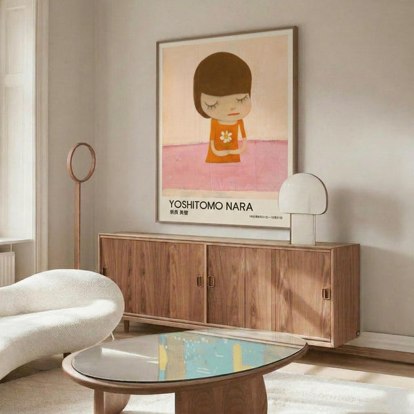 May include: A framed poster featuring a minimalist illustration of a young girl with brown bob haircut and closed eyes, wearing an orange dress with white flower, standing on a pink surface against a cream background. The artwork is displayed above a mid-century modern walnut credenza in a bright living room with white curved chair, oval glass coffee table, and contemporary lighting fixtures.