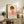 May include: Framed poster print featuring a minimalist illustration of a young girl with brown bob haircut and closed eyes wearing an orange dress with white flower, set against pink and beige color blocks, displayed on rustic wooden sideboard with decorative plants, books, and pottery in warm-toned living room setting.