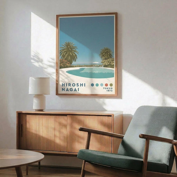 May include: A framed vintage-style poster showing a serene pool scene with palm trees and blue sky, displayed above a wooden mid-century modern credenza with sliding doors. A minimalist white ceramic table lamp sits on the credenza, and a gray upholstered armchair with wooden frame is positioned nearby. Warm natural light creates soft shadows on the white wall, giving the room a calm, retro aesthetic with teal and warm wood tones throughout.
