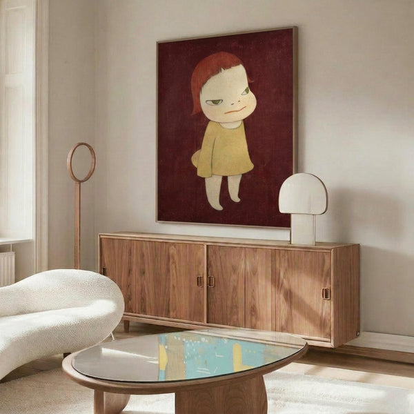 May include: Framed poster of a stylized child character with red-orange hair and yellow dress on deep burgundy background, displayed above a mid-century modern wooden credenza with sliding doors. Room features white curved chair, oval glass coffee table, white mushroom lamp, and brass floor mirror against cream walls with natural lighting.