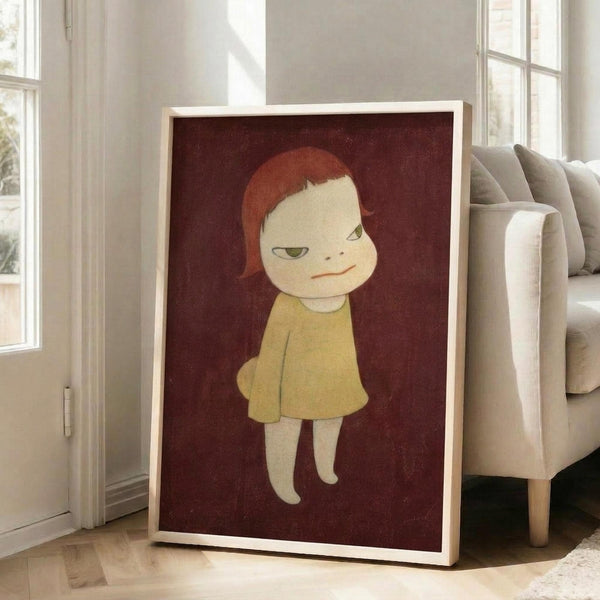 May include: Large framed poster leaning against white wall next to beige sofa in bright living room with windows. Artwork shows stylized child figure with red-orange hair wearing yellow dress against deep burgundy background. Simple illustration style with muted colors and minimal details. Light wood frame, approximately 3 feet tall based on furniture scale.