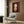 May include: Contemporary art print displayed in modern living room setting with beige armchair, geometric pillow, brass floor lamp, and dark wood paneling. Artwork shows stylized child figure with red-orange hair wearing yellow dress against deep burgundy background, housed in light wood frame.