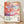 May include: Framed art poster leaning against white wall on light wooden floor. The artwork features abstract colorful whales or fish shapes in coral, pink, teal and purple with dotted patterns and flowing organic forms. Text reads "YAYOI KUSAMA Tokyo, Japan 1984" with Japanese characters below. Natural wood frame with clean modern aesthetic. Soft shadows cast on textured white wall behind.