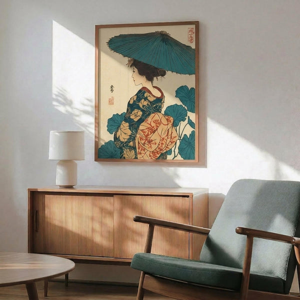 May include: Japanese ukiyo-e style artwork showing a woman in colorful kimono holding a teal umbrella, surrounded by large blue-green leaves. The print is displayed in a thin wooden frame on a white wall above a mid-century modern wooden credenza with sliding doors. A small white ceramic table lamp sits on the credenza, and a gray upholstered armchair with wooden frame is positioned nearby. Warm natural sunlight creates geometric shadows across the scene.
