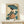 May include: Japanese woodblock print style artwork in wooden frame showing woman in profile wearing colorful floral kimono, holding teal blue parasol, surrounded by large lotus leaves. Print has cream background with red seal marks. Small white wrapped gift sits on light wood shelf below framed art against white wall.