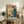 May include: Vintage-style poster with Japanese text and retro computer illustration displayed in wooden frame on rustic credenza beside potted fern, books, and ceramic vase in cozy living room with beige armchair and warm lighting