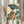 May include: Framed Japanese woodblock print showing a woman in profile wearing a colorful patterned kimono and holding a blue paper umbrella, surrounded by large teal lotus leaves. Person in cream ruffled sleeves holds the light wood frame against white curtains, with dried pampas grass visible on the left side of the image.
