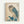 Japanese woodblock print featuring an owl with large yellow eyes perched on a branch with blue-green leaves. The owl has detailed brown and cream feathered plumage with turquoise-blue wings and back. Set against a cream background with traditional Japanese characters in the upper right corner and a red artist seal in the lower left. Displayed in a light wooden frame on a white wall.