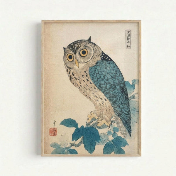 Japanese woodblock print featuring an owl with large yellow eyes perched on a branch with blue-green leaves. The owl has detailed brown and cream feathered plumage with turquoise-blue wings and back. Set against a cream background with traditional Japanese characters in the upper right corner and a red artist seal in the lower left. Displayed in a light wooden frame on a white wall.