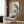 May include: Japanese woodblock print style artwork of an owl with blue and teal wings and cream colored body perched on flowering branch, displayed in light wooden frame on wood paneled wall above beige upholstered armchair with geometric patterned pillow, beside brass floor lamp and dark round side table with open book