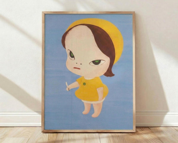 May include: Framed art print leaning against white textured wall on light wood floor. The artwork shows a stylized child-like character with an oversized head, brown bob haircut, yellow beret, and large green eyes against a soft blue background. The character wears a yellow dress with green button and has pale skin with rosy cheeks. Natural wood frame surrounds the print, with soft lighting creating gentle shadows on the wall.