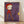 May include: Framed art print leaning against white wall on light wood floor. Features stylized character in red hooded outfit and cap standing on wooden stilts, holding fishing rod with yellow cylindrical object dangling from line. Purple watercolor background. Pale complexion, blonde hair, minimalist facial features. Light wood frame. Soft natural lighting creates gentle shadows on wall.