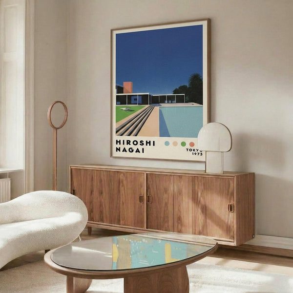 May include: Mid-century modern living room with wooden sideboard, white curved chair, and glass coffee table. Framed poster on wall shows modernist architecture with swimming pool, lawn, and blue sky in retro illustration style. Warm wood tones throughout room with natural lighting and minimalist decor including brass floor lamp and table lamp.