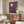May include: Contemporary art poster featuring a stylized child character in red hooded outfit walking on stilts against purple background with small yellow lantern, displayed above wooden sideboard in modern living room with white curved chair, glass coffee table, and minimalist table lamps