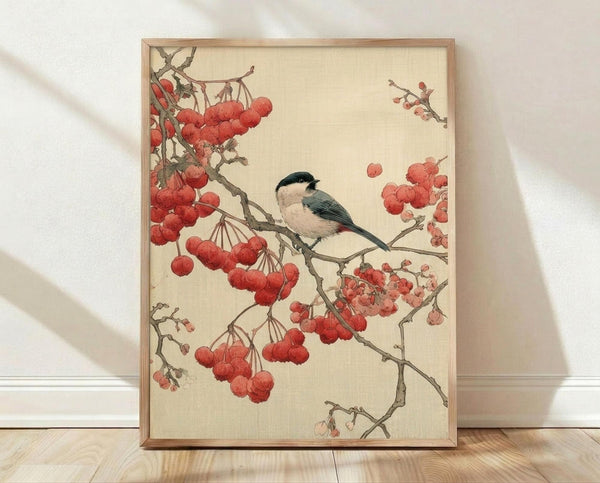 May include: Framed vintage Japanese-style artwork featuring a small bird with black cap and cream breast perched on branches heavy with bright red berries. The illustration has warm beige background with delicate botanical details. Light wood frame rests against white wall on wooden floor with soft natural lighting casting shadows.