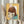 May include: Person holding framed artwork showing cartoon-style illustration of young girl with brown bob haircut and large yellow-green eyes, created on collaged vintage documents and papers in pink, blue, and yellow tones. Dried wheat stems visible on left side of neutral-toned room setting.