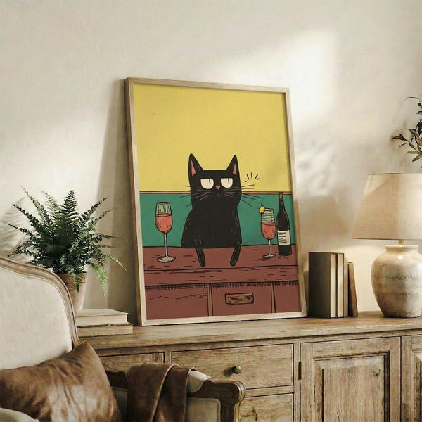 May include: Framed poster print featuring a black cat with yellow eyes sitting on a wooden surface between two wine glasses and a wine bottle, with yellow and teal background colors. Displayed on rustic wooden sideboard with books, ceramic vase, and fern plant in modern living room setting with beige couch.
