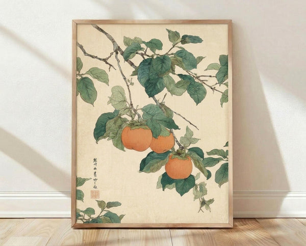 May include: Framed botanical print showing orange persimmons hanging from leafy green branches in traditional Japanese woodblock style, displayed in light wooden frame against white textured wall on wooden floor with soft natural lighting and shadows