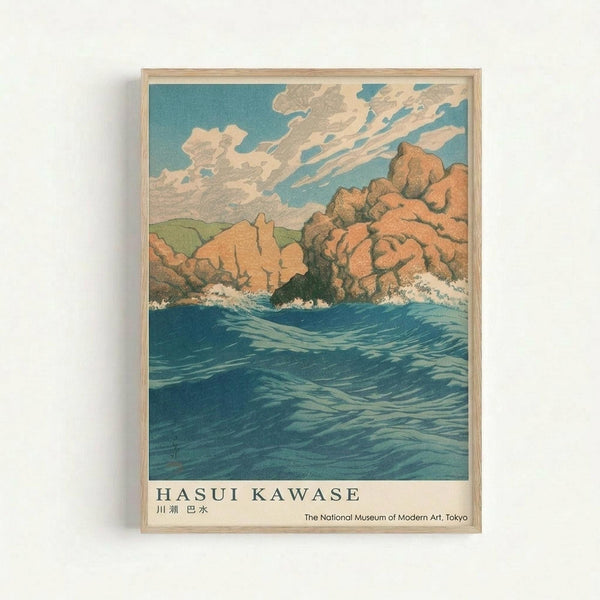 Vintage Japanese woodblock print style artwork showing dramatic blue ocean waves crashing against orange and tan colored rocky cliffs. A turquoise sky filled with white and gray clouds stretches across the top. The print features bold colors and traditional Japanese artistic techniques. Text at bottom reads "HASUI KAWASE" with Japanese characters and "The National Museum of Modern Art, Tokyo." The artwork is displayed in a light wooden frame against a white wall.