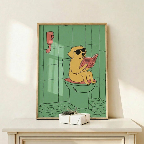 May include: Framed cartoon poster showing golden retriever wearing sunglasses sitting on green toilet reading pink newspaper in tiled bathroom. Light wood frame displayed on white shelf next to small wrapped gift with twine bow against cream wall.