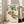 May include: Framed botanical artwork leaning against white wall next to beige sofa, showing orange persimmons hanging from green leafy branches in traditional Japanese watercolor style on cream background, with Asian calligraphy and red seal stamp in lower left corner, displayed in light wood frame on hardwood floors near large windows