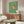 May include: Framed poster artwork showing a golden retriever wearing sunglasses sitting on a toilet while reading a red book, set against green tiled bathroom walls. The cartoon-style print is displayed above a mid-century modern walnut credenza in a contemporary living room with white walls, white upholstered chair, oval glass coffee table, and modern lighting fixtures.