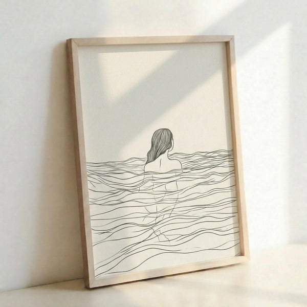 May include: Minimalist line drawing artwork in light wooden frame leaning against white wall. Black ink illustration shows woman's head and shoulders emerging from wavy water lines on cream background. Simple, flowing linework creates ocean waves throughout composition. Natural lighting casts soft shadows on frame and wall.