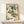 May include: Vintage Japanese botanical art print in thin gold frame showing orange persimmons hanging from green leafy branches with calligraphy, displayed on light wood console table next to small white wrapped gift with natural twig decoration against cream wall