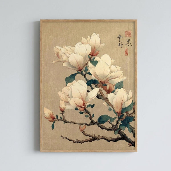 May include: Framed botanical art print hanging on white wall showing magnolia branch with pale cream and pink blossoms against warm beige background. Traditional Asian-style painting with delicate brushwork, dark twisted branches, and green leaves. Natural wood frame. Japanese calligraphy and red seal stamps in upper right corner.