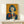 May include: Framed vintage Japanese Coca-Cola advertisement poster featuring woman with black bob haircut and red lips holding glass Coke bottle against yellow background with red Japanese text, displayed on light wood console table next to small white wrapped gift with dried grass decoration