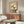 May include: Japanese-style botanical artwork featuring white magnolia blossoms on beige background, displayed in thin wooden frame above mid-century walnut credenza. Room shows cream curved chair, brass floor lamp, oval glass coffee table with colorful reflective surface, and white walls with natural lighting.