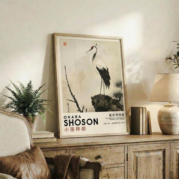 May include: Framed vintage Japanese art print featuring a white crane with black wing tips and red crown standing on a dark rock, displayed on rustic wooden sideboard alongside fern plant, ceramic vase, books, and table lamp in neutral-toned living room setting