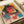 A vibrant cyberpunk-style art print featuring a woman with dark hair wearing round sunglasses, rendered in bold pink, yellow, and teal colors with digital glitch effects and Japanese text elements. The poster lies flat on white paper with a tape dispenser visible nearby, showing the print's square format and retro-futuristic aesthetic with geometric patterns and technological imagery overlaid throughout the composition.