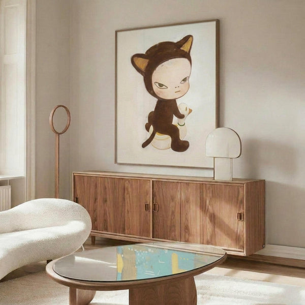 May include: Framed poster featuring a stylized cartoon character in a brown cat costume with pointed ears and yellow accents, displayed above a mid-century modern wooden sideboard. The artwork shows a pale-faced figure in a minimalist art style against a white background. Room setting includes a white curved chair, oval glass coffee table with colorful abstract design, white mushroom-shaped table lamp, and neutral beige walls with natural lighting.