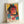 May include: Framed poster print leaning against white wall showing stylized woman with round glasses and dark hair in cyberpunk aesthetic. Artwork features vibrant yellow, pink, and teal color blocks with Japanese text characters, geometric shapes, and layered collage elements. Light wood frame surrounds the colorful digital art piece in modern interior setting.