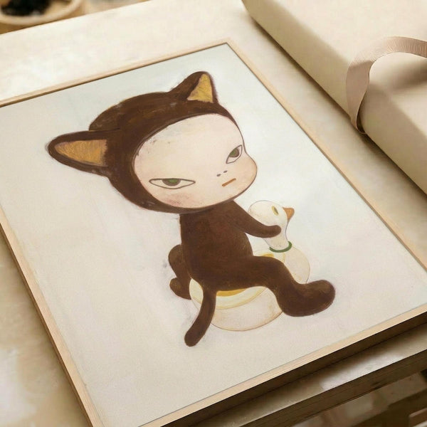 Whimsical illustration of a cat-like character with brown hood and pointed ears, pale face with green eyes, riding a white duck. The artwork is displayed in a light wooden frame on white paper, photographed at an angle on a neutral surface with soft lighting. The style is minimalist and childlike with muted earth tones.