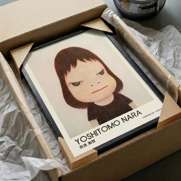 May include: Framed art print featuring minimalist illustration of a young girl with brown bob haircut and green eyes against cream background, displayed in black frame inside cardboard shipping box with protective wrapping materials and wooden dowels