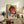 May include: Framed cyberpunk artwork featuring a woman with round sunglasses and headphones in vibrant pink, yellow, and teal colors with Japanese text elements, displayed on a rustic wooden console alongside books, a potted fern, and ceramic vase in a modern living room setting with white walls and upholstered furniture.