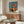 May include: Vintage Japanese poster featuring woman in yellow dress holding orange parasol beside orange car on beach, displayed above wooden credenza in modern living room with white curved chair, glass coffee table, and warm natural lighting